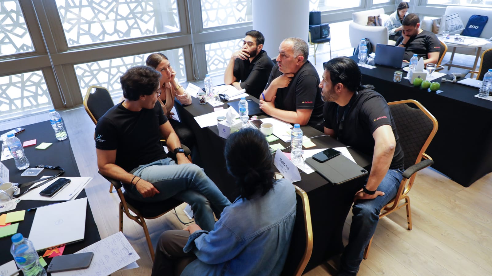 A working session in progress around a long table, daylight from full-height windows